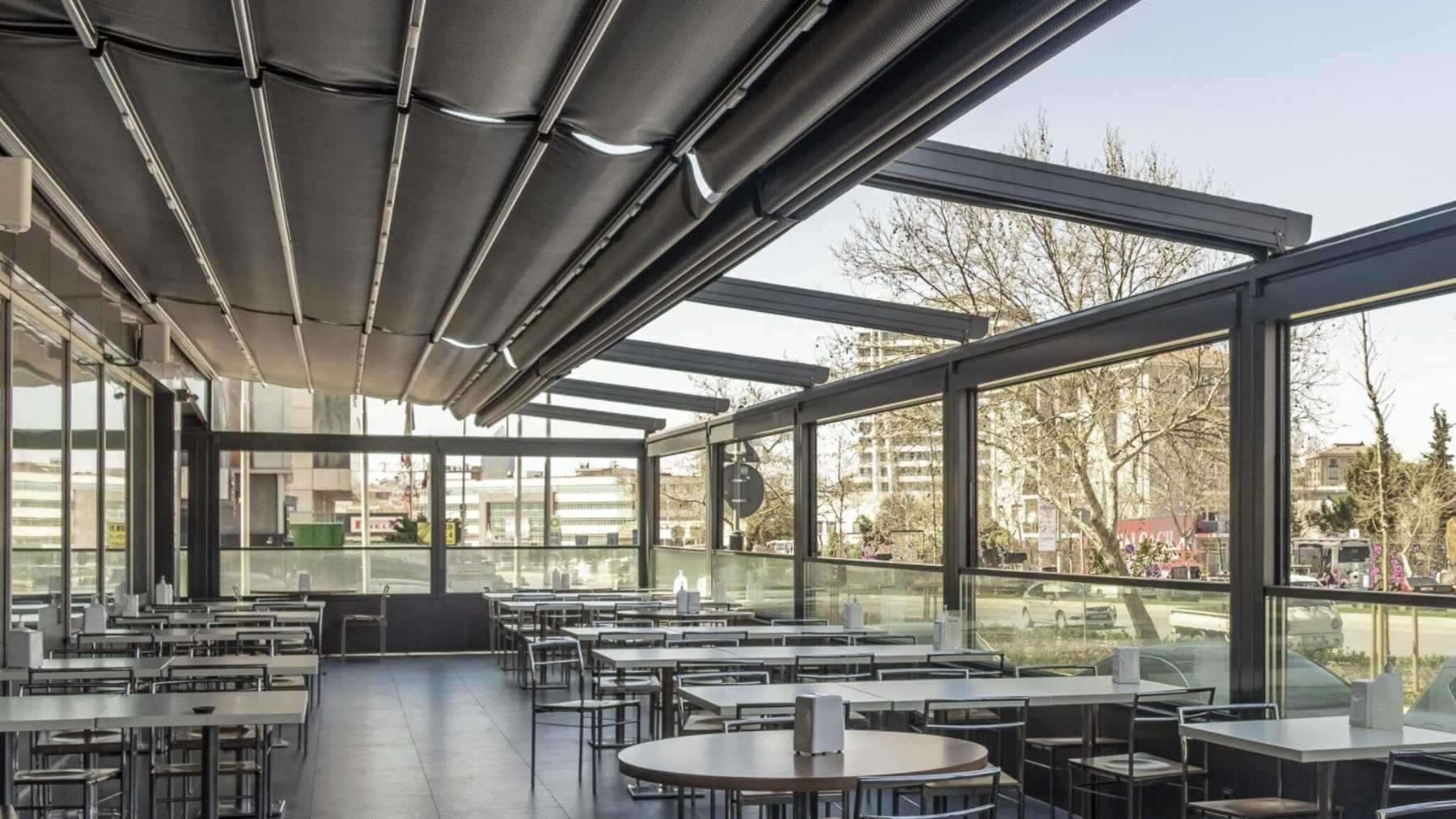 Pergolë me çati të tërheqshme dhe xhama anësorë në një restorant